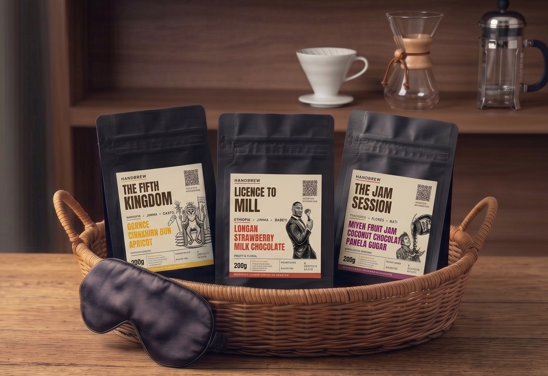 Three coffee packages in a basket with a sleep mask on a wooden surface, a v60, chemex, and a cafetiere in the background.
